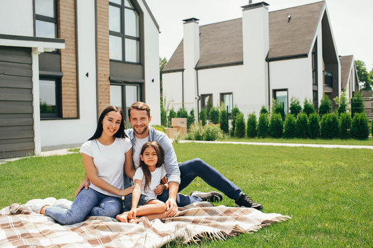 Happy Heteroseksual Family Sitting On Grass Near Their New House. Family Sitting On Lawn, Buying New Big Home .