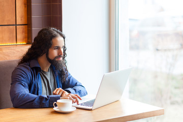 Portrait of handsome intelligence bearded young adult man freelancer in casual style sitting in cafe and searching information for work in laptop, bussinessman in office. Indoor, lifestyle concept