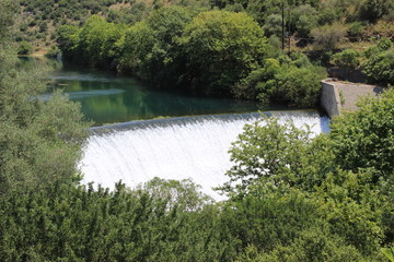 Water spills over the top of Louros river hydroelectric dam in a green forest in Epirus, Greece near the town of Filippiada