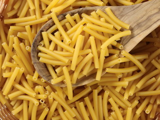 Macaroni, raw pasta in wooden food basket with spoon, top view