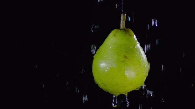 Close up shot of water droplets falling on green pear floating on black background