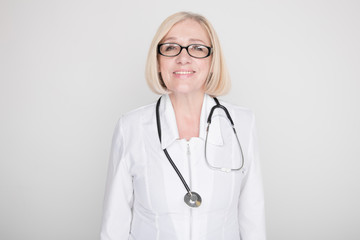 Woman doctor in glasses standing with stethoscope and looking in camera in a studio