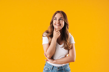 Cheerful happy girl in casual white t-shirt posing isolated over yellow wall background looking aside.