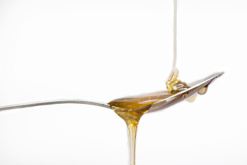 Honey dripping from a silver spoon on isolated white background