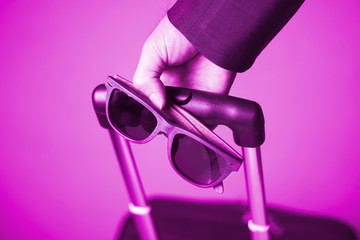 Pink theme on businessman 's hand holding sunglasses and drag travel bag,travel concept.