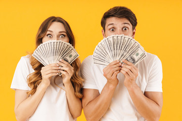 Portrait of happy couple man and woman in basic t-shirts rejoicing while holding bunch of dollar...
