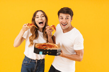 Portrait of caucasian couple man and woman in basic t-shirts smiling while eating pizza from box