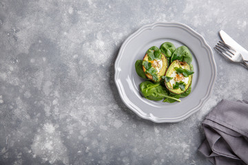 Quail eggs baked in avocado. Avocado egg boats served with spinach leaves on gray plate . Ketogenic, keto low carb diet. Food background. Top view. Copy space.