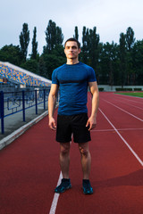 Yong handsome male stands on the stadium in blue outfit in the morning
