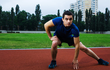 Obraz premium Young man stretching and preparing on the stadium in blue shirt