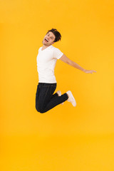 Full length photo of cheerful man in basic t-shirt rejoicing and jumping with spreading arms aside