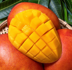 Fresh juicy beautiful diced mango fruit in bamboo basket on green leaves background, top view,...