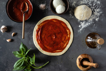 Ingredients for traditional Italian pizza Margherita with tomato sauce, Mozzarella cheese, basil on a dark concrete background. Top view. Pizza recipe and menu. View from above. Space for text.