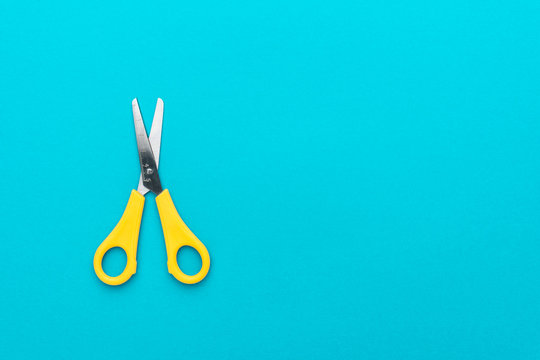 minimalist photo of yellow children's scissors on the turquoise blue background. flat lay shot of opened yellow scissors with copy space