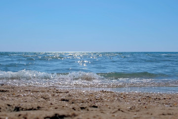 Fototapeta na wymiar Sea coast on sand beach on Sunny day. Sun's rays are reflected on sea surface. Background.