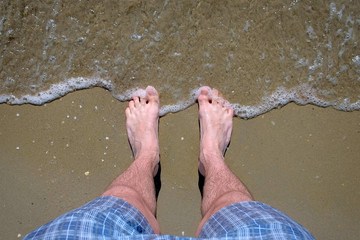 Man stands barefeet on sandy beach on warm Sunny day. Waves roll back and forth. Concept of...