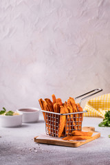 Homemade baked sweet potato french fries with ketchup, salt on wooden board with parchment