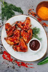 grilled chicken wings with tomato sauce on white plate on grey background top view