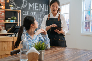 Waitress using digital tablet while taking order at bar restaurant. girl barista repeat meal to customer to check again in modern coffee shop. female client concentrated listening to staff in cafe.