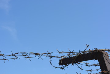 Black metal fencing with barbed wires against thieves in the blue sky.