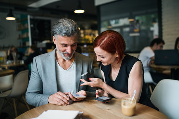 Man and woman having business meeting in a cafe, using smartphone.