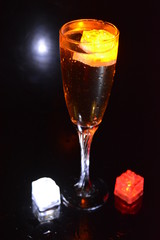Multicolored glowing ice cubes float in a crystal champagne glass that illuminates the drink in it.