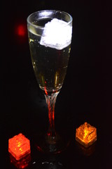 Multicolored glowing ice cubes float in a crystal champagne glass that illuminates the drink in it.