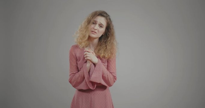 Caucasian girl pleads and makes sorrowful expression on grey background