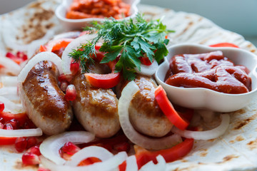 Fried pork sausages on pita bread with ketchup and Armenian appetizer Aivar with vegetables. Lavash, red bell pepper, onions, sausages. Oktoberfest food, the concept of the pub