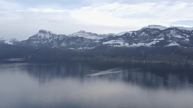 Aerial drone shot of a barge sailing across a lake surrounded by snow covered mountains and trees
