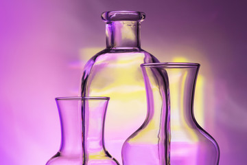 glass transparent tableware - bottles of different sizes, three pieces on a beautiful multi-colored, yellow, lilac and pink, background. very beautiful still life. close up.