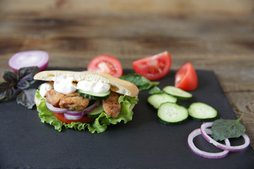 Closeup. Pita - sandwich, sabiche stuffed with chicken, tomatoes, cucumbers, salad on a black plate and wooden background decorated with vegetables. Middle Eastern cuisine. With copy space for text.