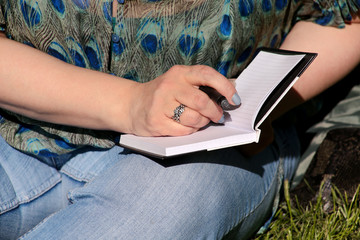 Woman and student sitting on grass, takes notes in notebook, learning and writes thoughts, writes book, she is preparing his final exams doing homework and thinking, writing something in his notebook.