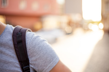 One shoulder man with strap of backpack with street view on the backgound and sunset lights close up