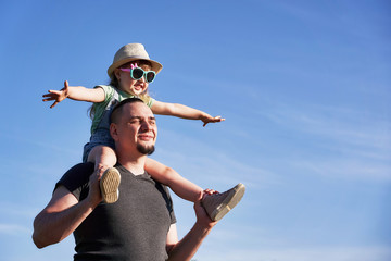 father and daughter on shoulders happily rejoice. dad holding little daughter sitting on mimics the...
