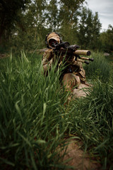 Portrait airsoft soldier with a rifle playing strikeball in outdoor in grass