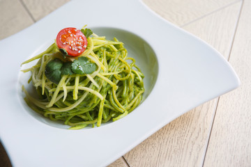 green spinach spaghetti with cheese and tomato on wooden table