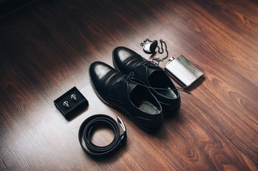 Obraz na płótnie Canvas Leather shoes, a belt, a flask of whiskey, antique watches lie on a wooden parquet. Wedding men's set and details. Photography and concept.
