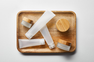 top view of few empty jars and cream tubes on wooden tray on white