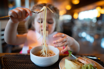 Litle girl is eating pasta in the restaurant.
