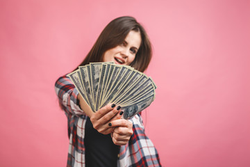 Portrait of a cheerful young woman holding money banknotes and celebrating isolated over pink background.