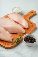 Raw uncooked chicken fillet on a cutting table with ingredients for cooking