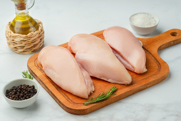 Raw uncooked chicken fillet on a cutting table with ingredients for cooking