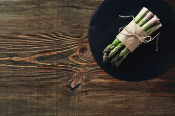An edible, raw stems of asparagus on a wooden background.
