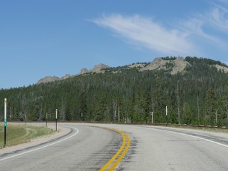 Cropped sharp curve in the road along forests and hills at Bighorn National Forest in Wyoming.