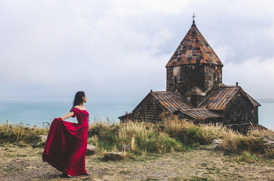 Portrait of young woman in red dress standing near monastery, Armenia