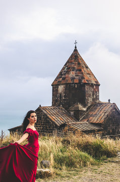 Portrait of young woman in red dress standing near monastery, Armenia