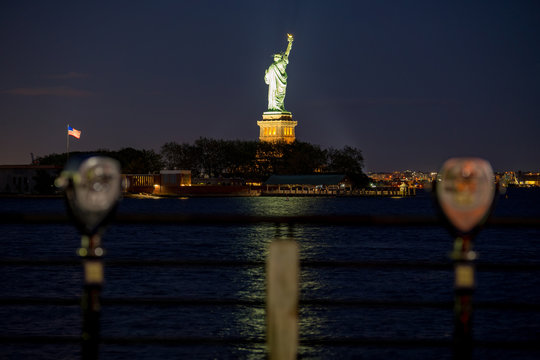 Night photo Statue of Liberty with blurry viewing binoculars in the foreground