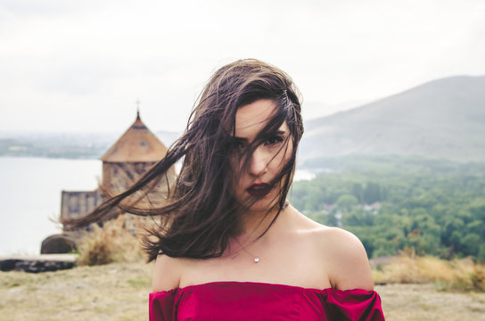 Portrait of young woman in red dress standing near monastery, Armenia