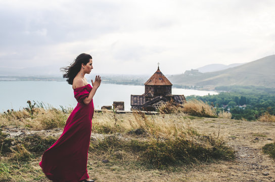 Portrait of young woman in red dress standing near monastery and pray, Armenia